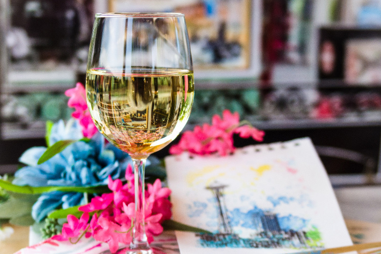 Sip n Sketch Image of Glass of White Wine and a painting on paper sitting on a desk with flowers